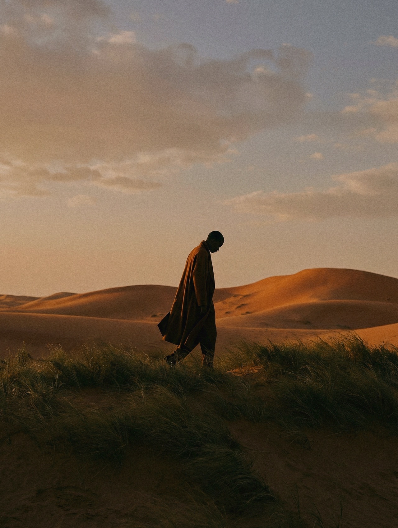 A solitary figure walking through golden desert dunes at dusk — the caravan moved on.
